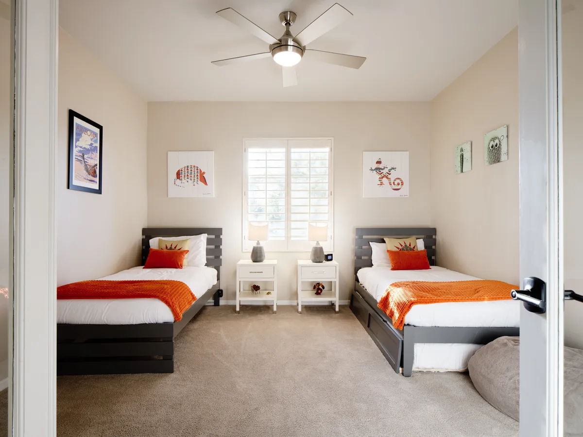 A cheerful bedroom featuring two twin beds with colorful artwork on the walls and nightstands with lamps, creating a playful yet restful environment suited for younger guests or flexible sleeping arrangements.