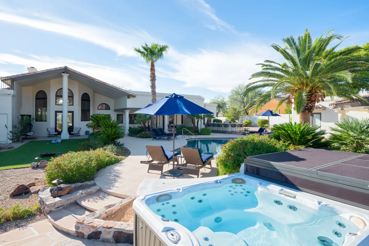 A serene outdoor scene featuring a shimmering swimming pool, a bubbling hot tub, palm trees, and comfortable lounge chairs. The space is designed for relaxation and socializing, ideal for unwinding after a day of activities.
