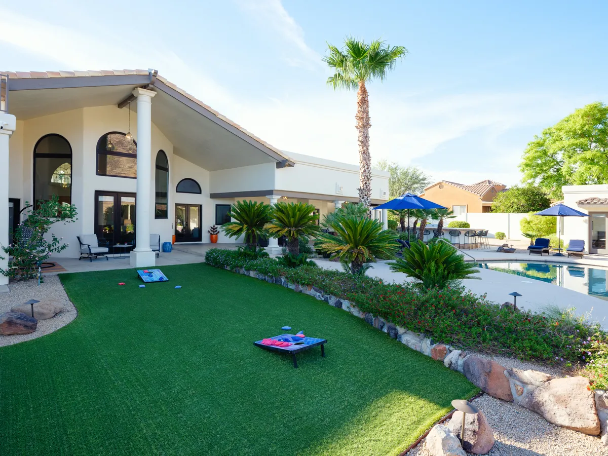 A vibrant exterior scene featuring a sparkling swimming pool, lush lawn area, palm trees, inviting outdoor seating, and landscaped gardens. The setup is perfect for both lounging in the sun and gathering with friends or family, with the pool serving as the focal point for leisure and socializing.