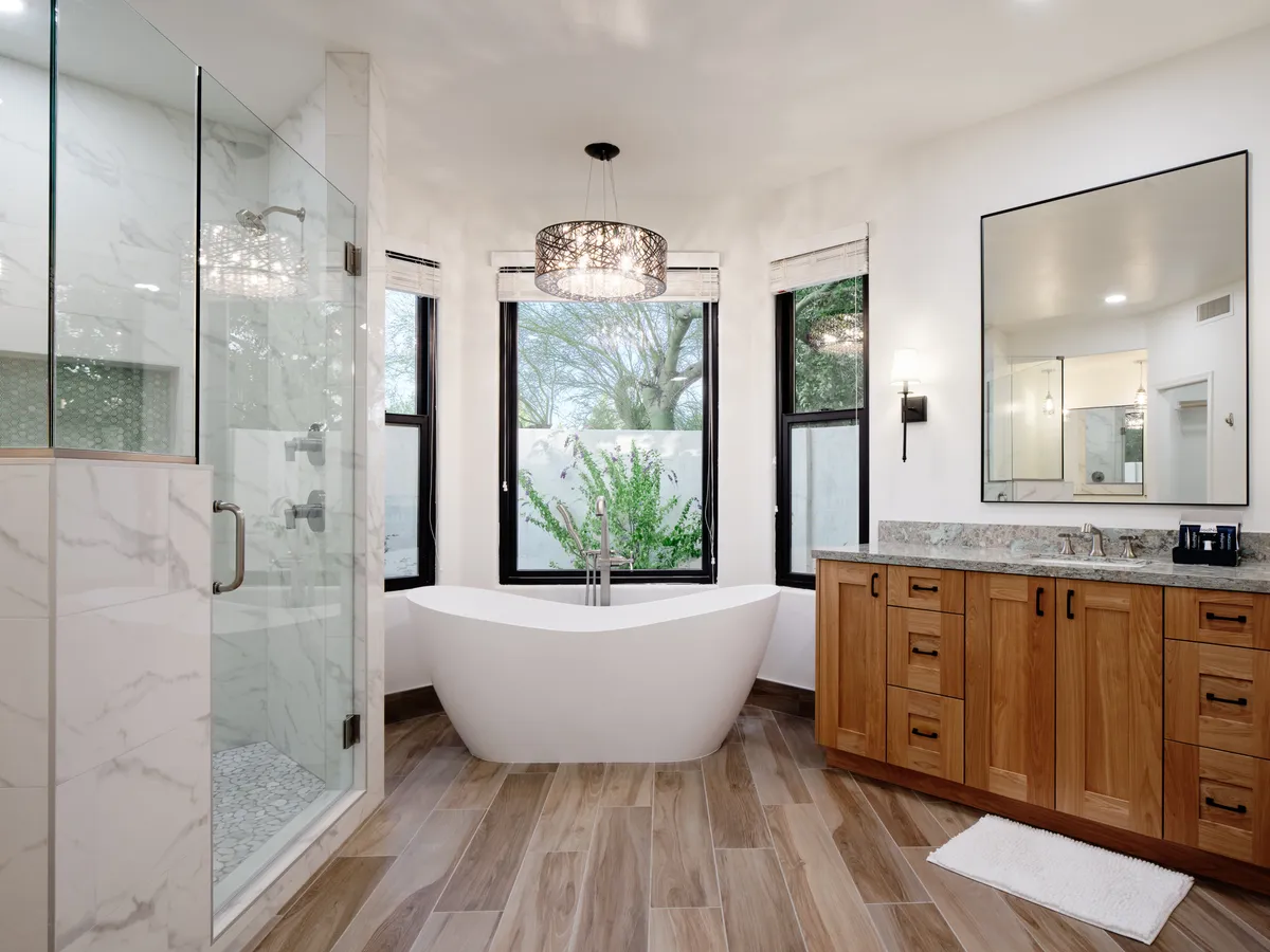 A spa-inspired bathroom with a freestanding tub, large windows, a vanity with wooden cabinetry, and a separate shower enclosure, flooded with natural light for a rejuvenating atmosphere.