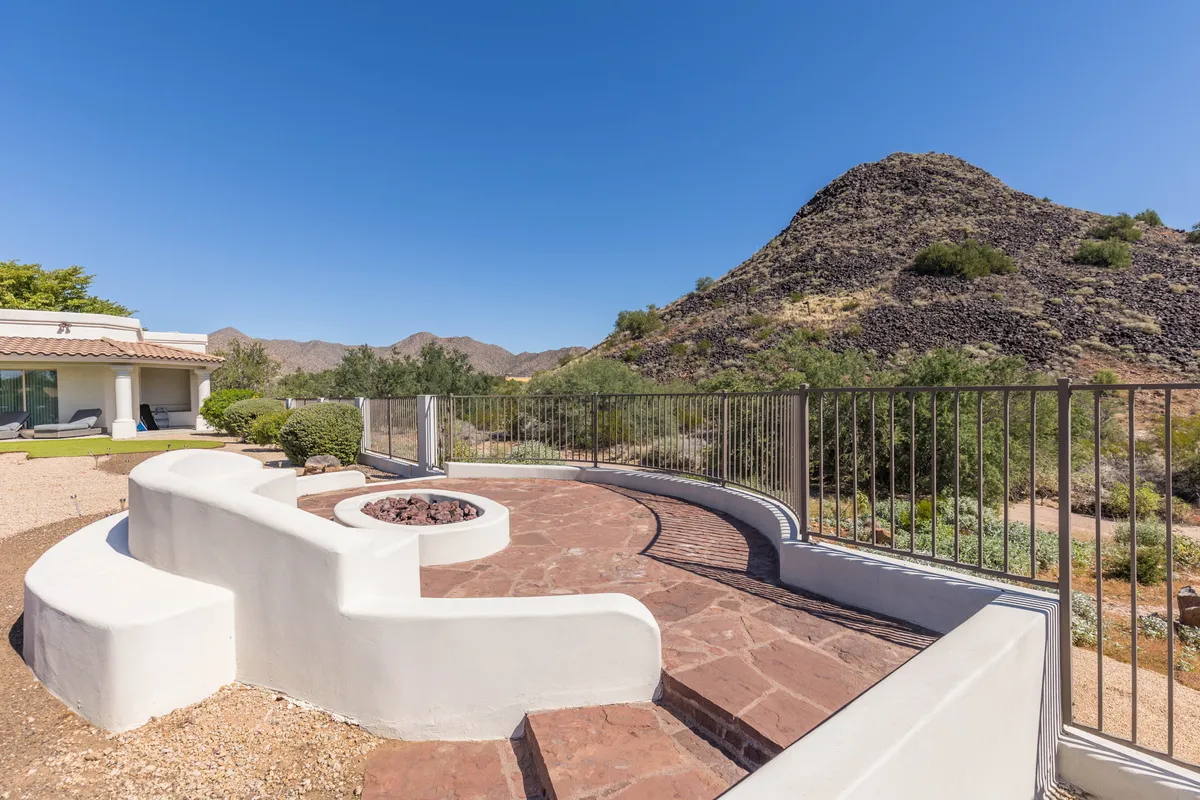 A cozy fire pit area with curved seating facing a stunning mountain backdrop. The space is designed for gatherings, with ample seating and an atmosphere perfect for stargazing or warming up on cool desert evenings.